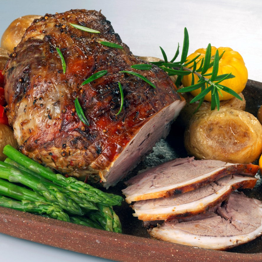 Scotch PGI Lamb Easter Roast, cooked with fresh rosemary, potatoes and spring asparagus on a wooden board